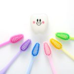 Aerial view of a rainbow of toothbrushes pointing toward a smiling tooth