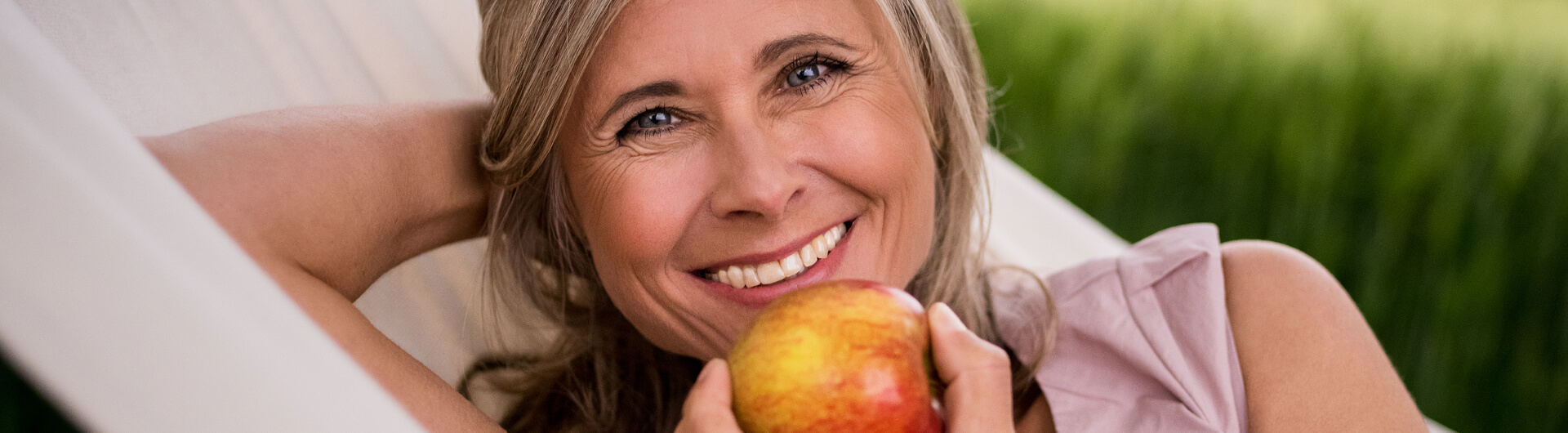 woman smiling and holding up an apple